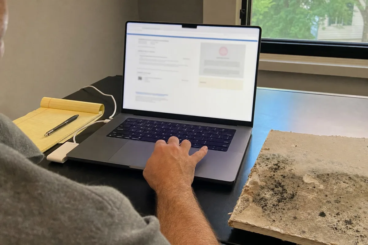 A homeowner checks a credential beside a mold stained drywall sample.
